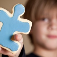 A 9 year old boy holding out a blue iced puzzle piece shaped sugar cookie.  Shallow DOF, focus on cookie only.
